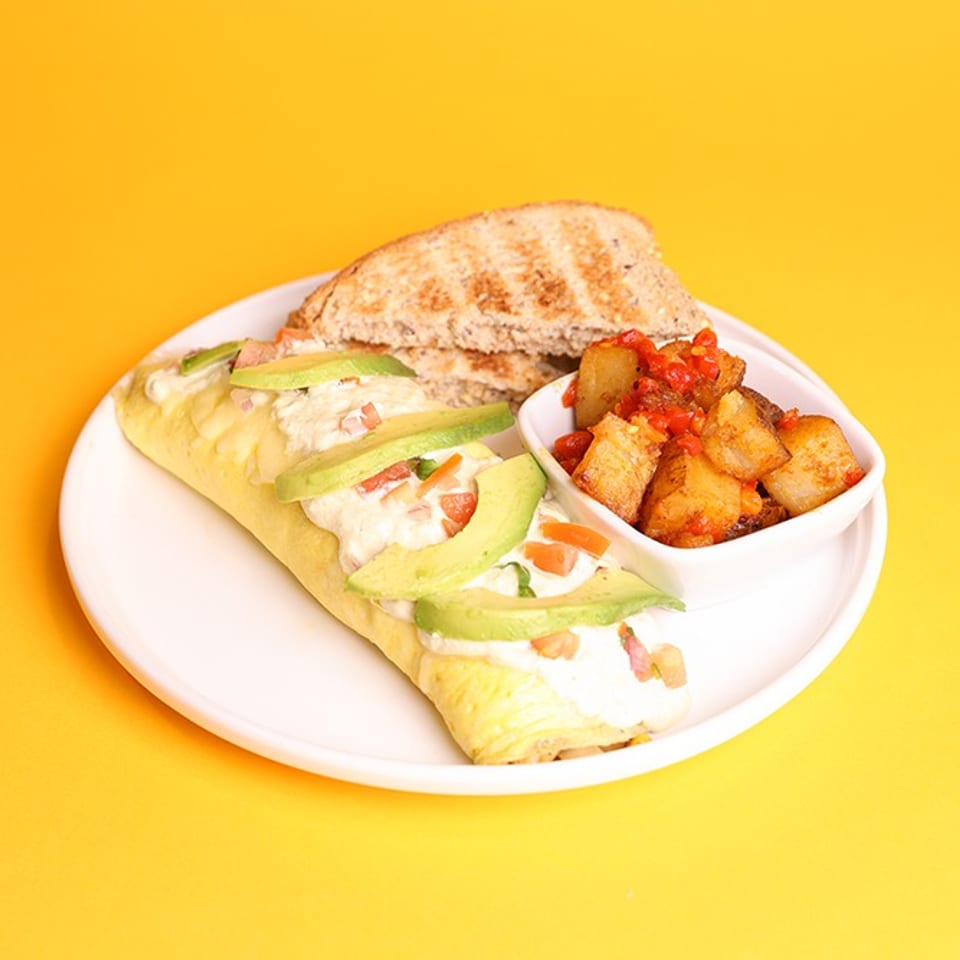 Grilled sandwich filled with avocado, creamy sauce, tomatoes, and bacon served with roasted potatoes and red salsa on a white plate.