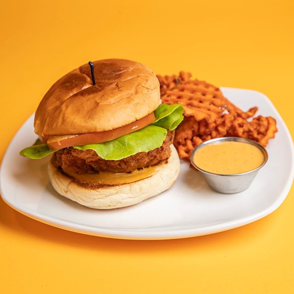 Crispy chicken sandwich with lettuce and tomato, waffle fries, and dipping sauce on a white plate.
