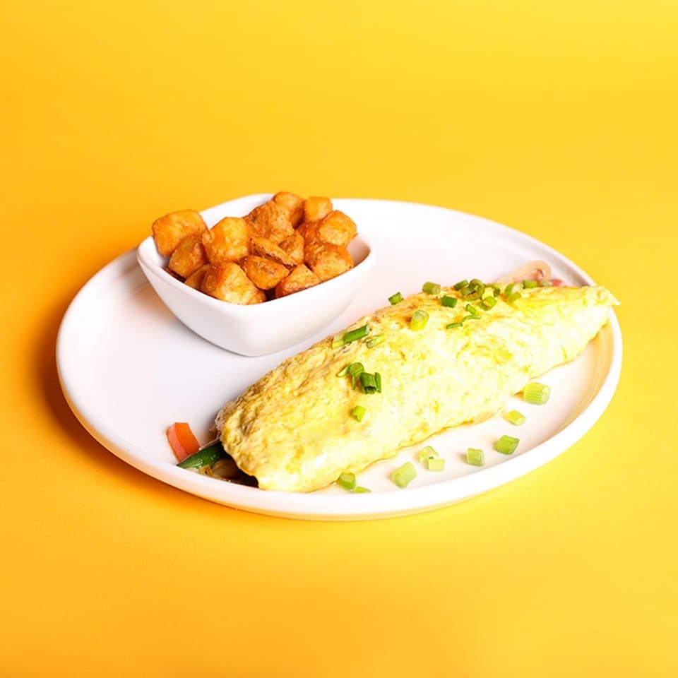 Omelet topped with chopped green onions, served with golden breakfast potatoes on a white plate against a yellow background.